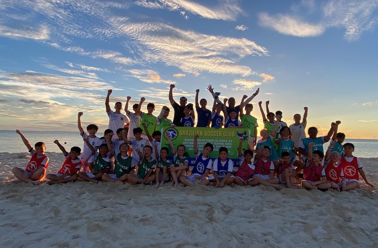 BSC Summer Camp 2025 — campers and coaches cheering on the beach at sunset with the club banner