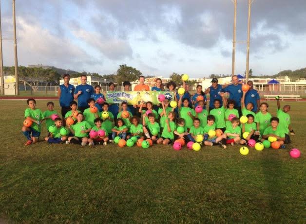BSC Summer Camp 2014 — campers in green shirts with colorful balls and coaches holding the Soccer Camp Okinawa banner